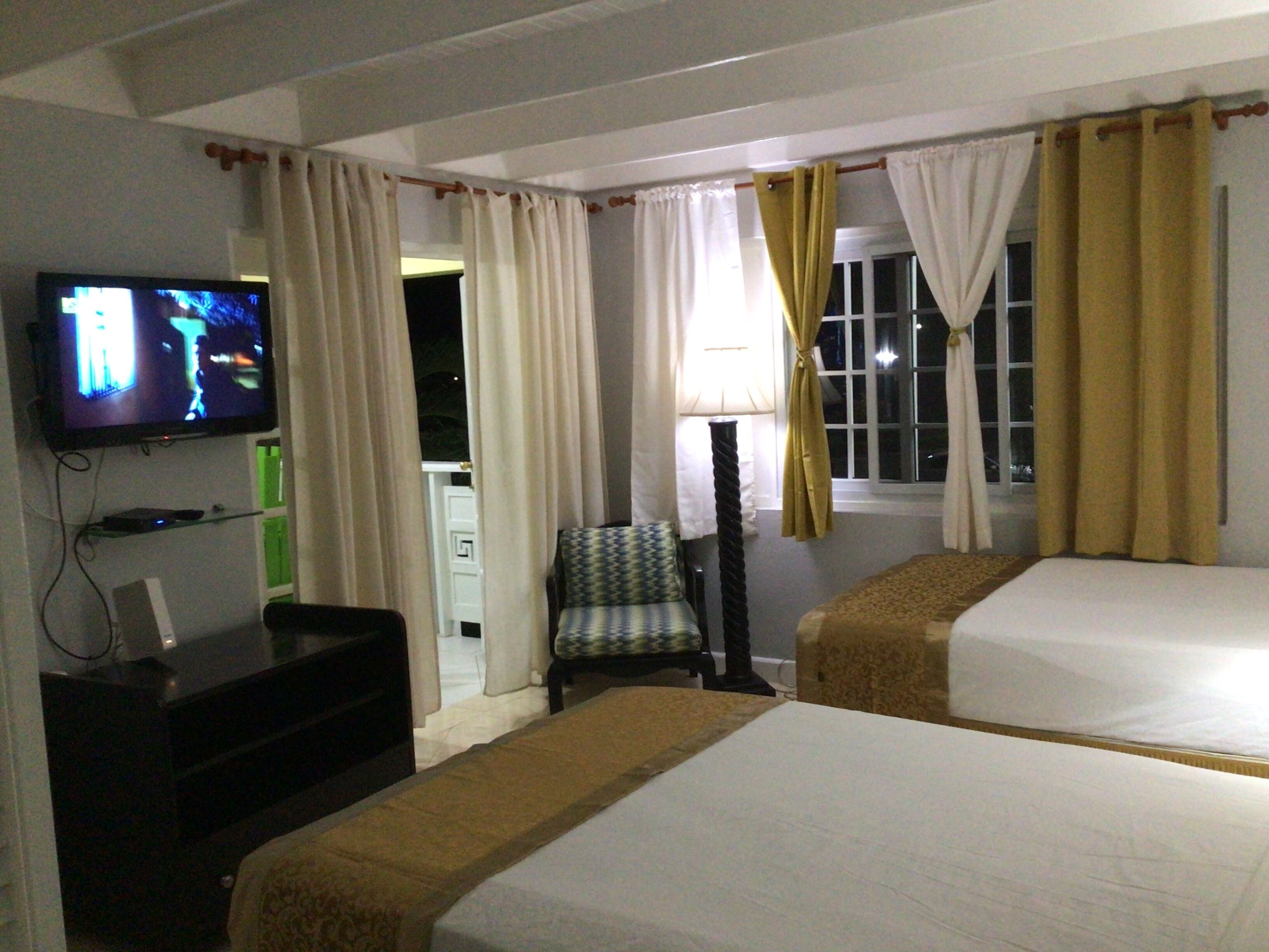 A hotel room with two beds, a television, a chair, and a window with curtains.