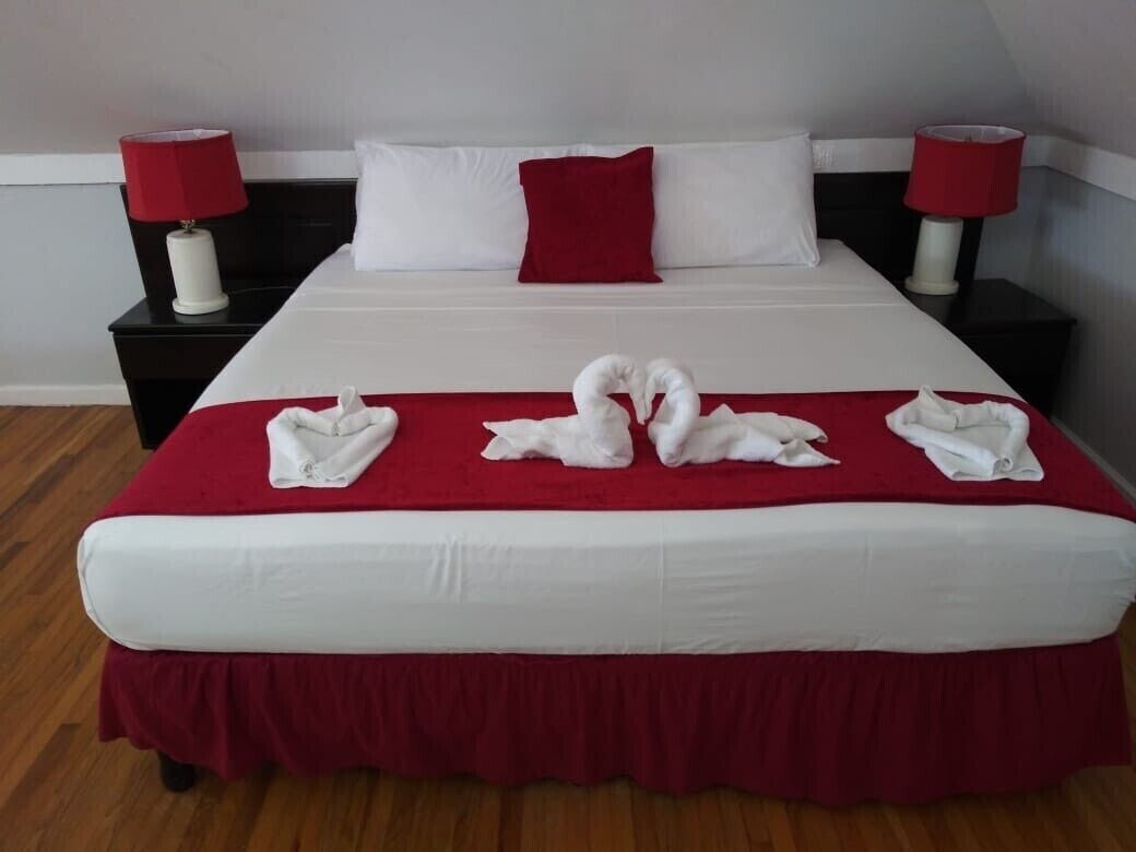 A neatly made bed with a red bedspread and white pillows, two red lamps on nightstands, and a red throw pillow on the bed.