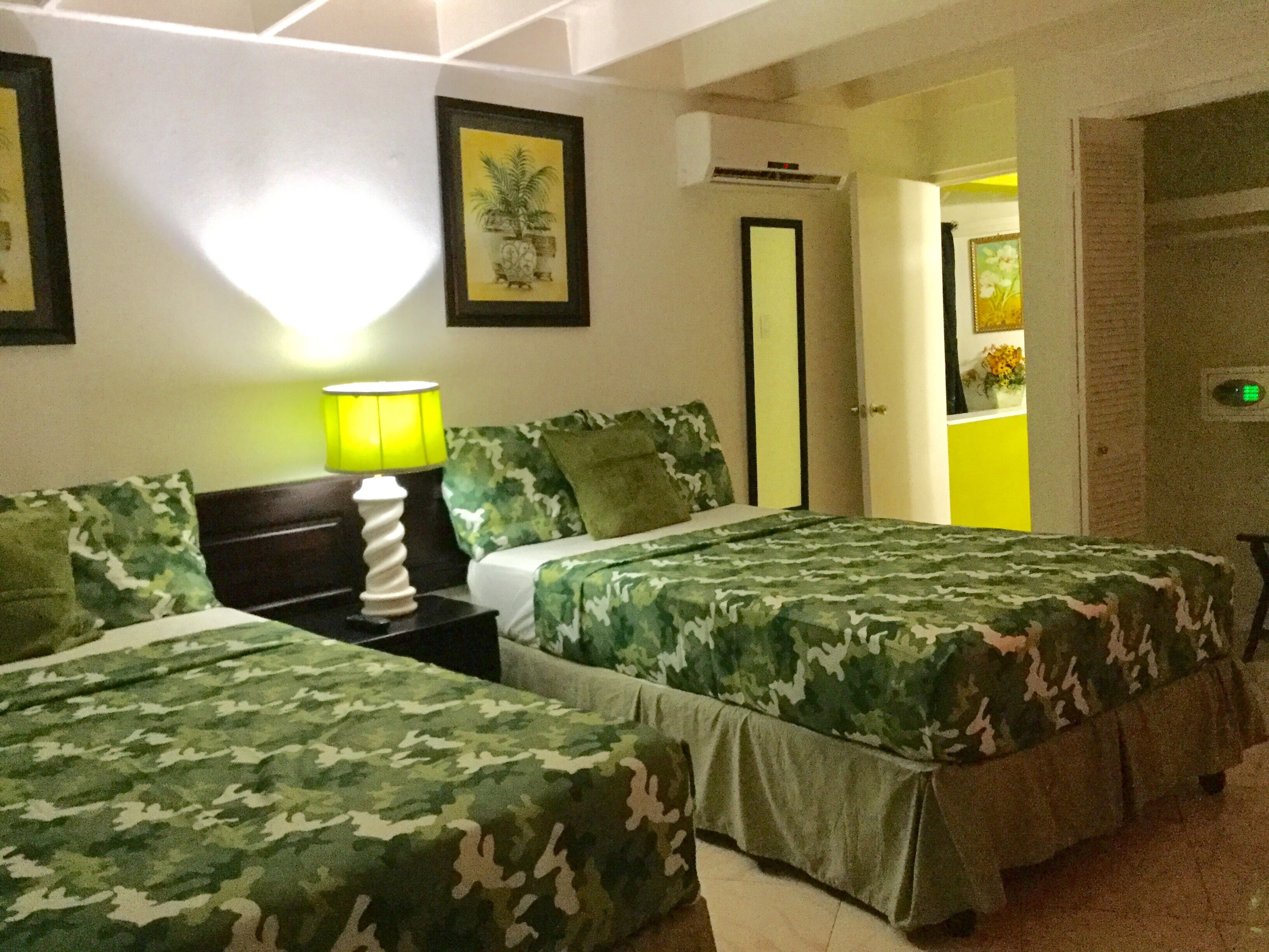Une chambre avec deux lits, chacun agrémenté de draps à motifs camouflage, d’une lampe de chevet et d’un tableau encadré au mur.