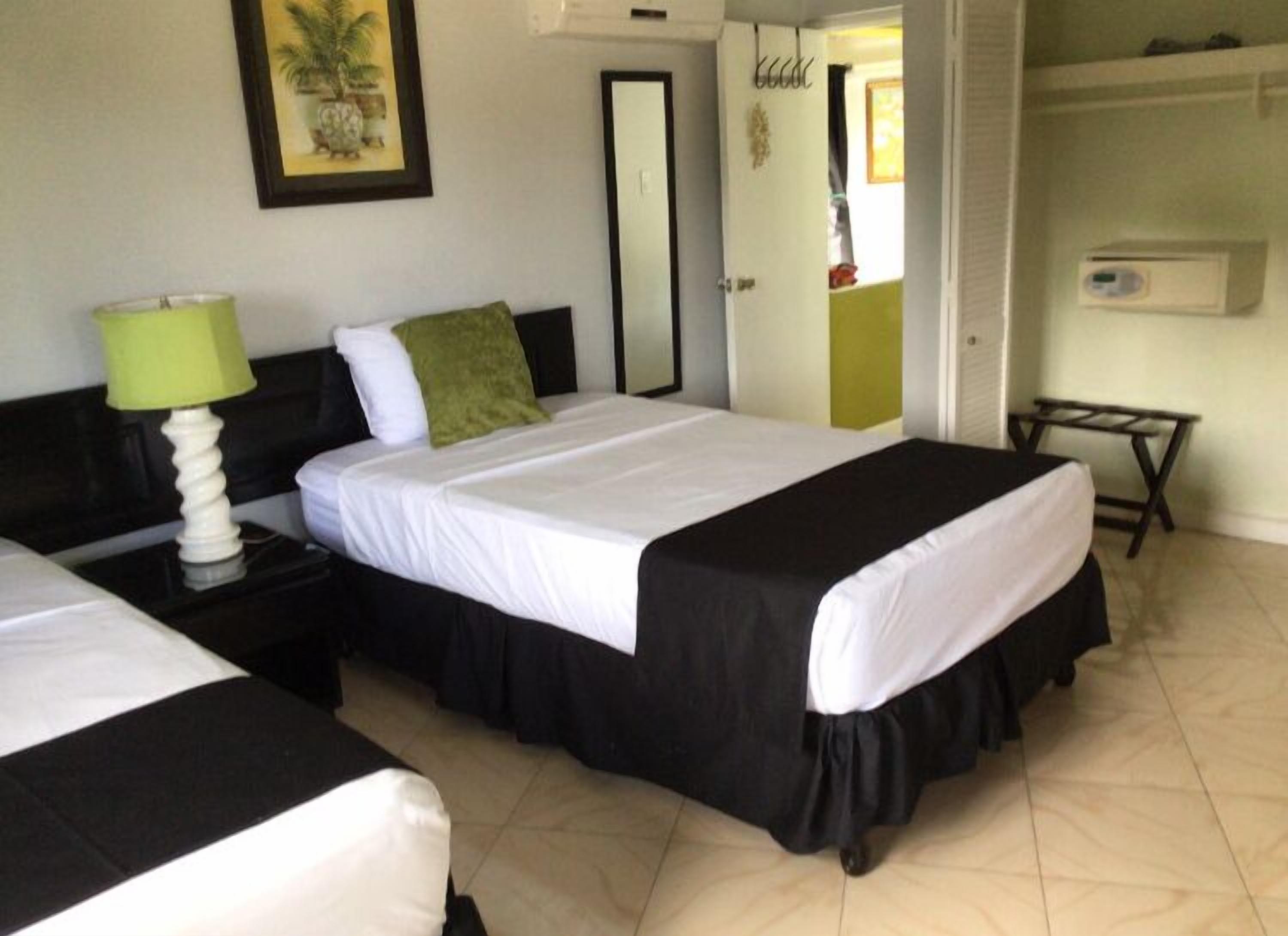 A hotel room with two beds, a nightstand with a lamp, a mirror, a wardrobe, and a small table.