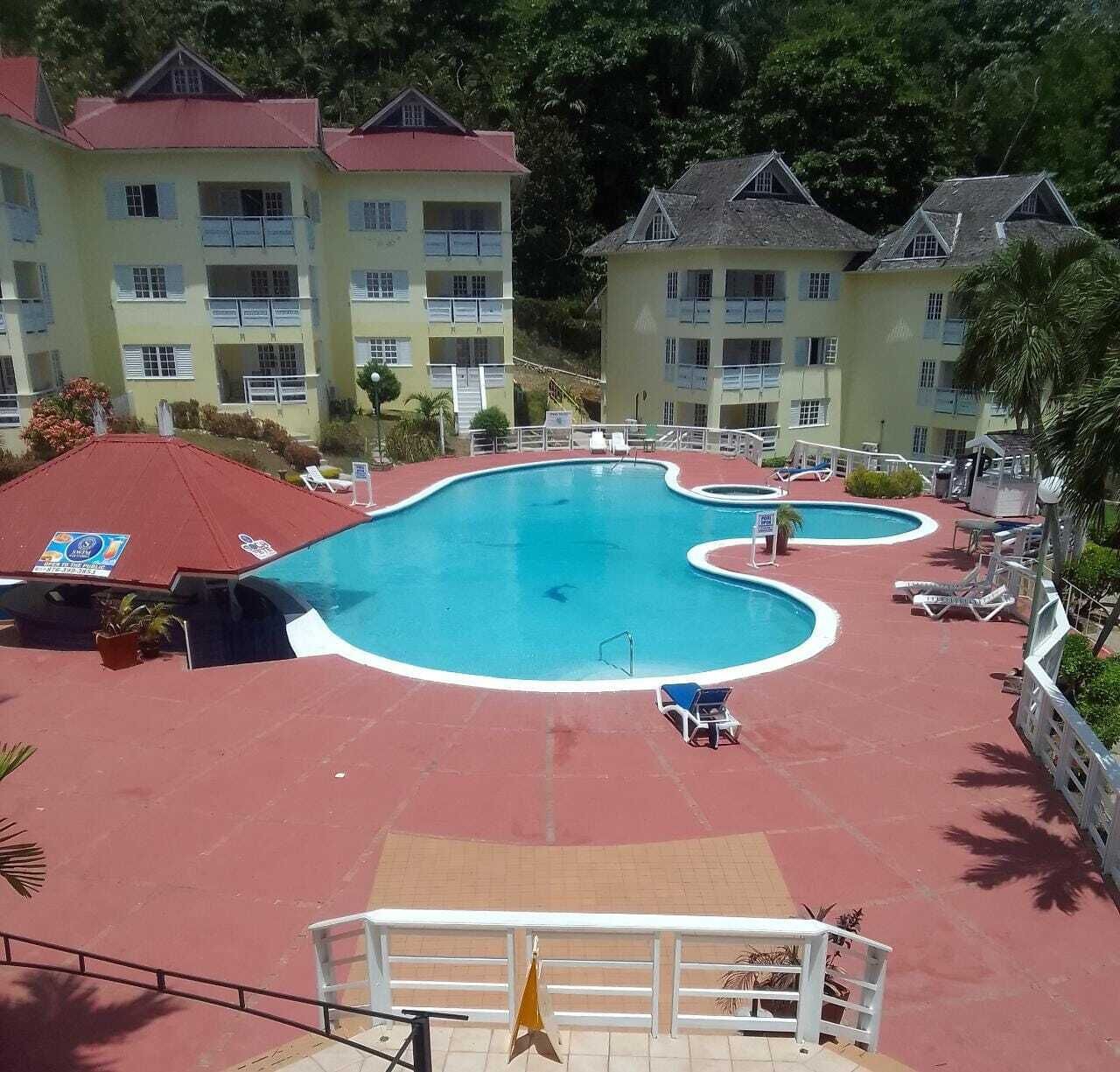 A hotel with a large swimming pool, multiple balconies, and a red-roofed building.