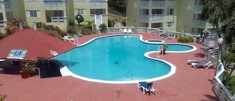 A hotel with a large swimming pool, multiple balconies, and a red-roofed building.