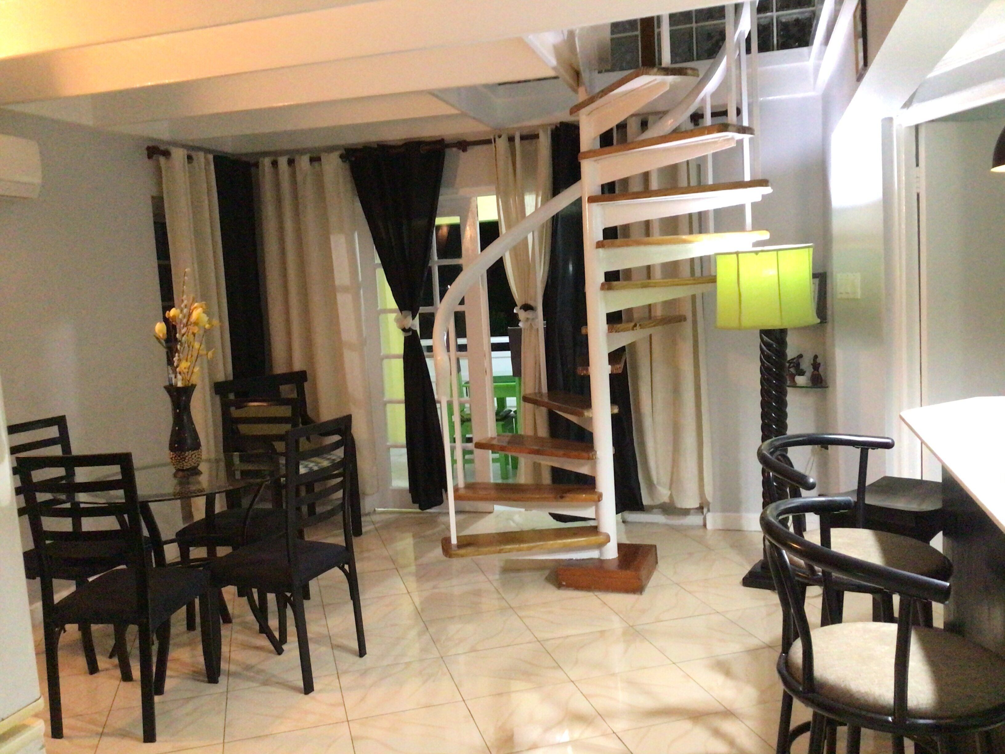 A dining area with a spiral staircase, a dining table with chairs, and a vase with flowers.