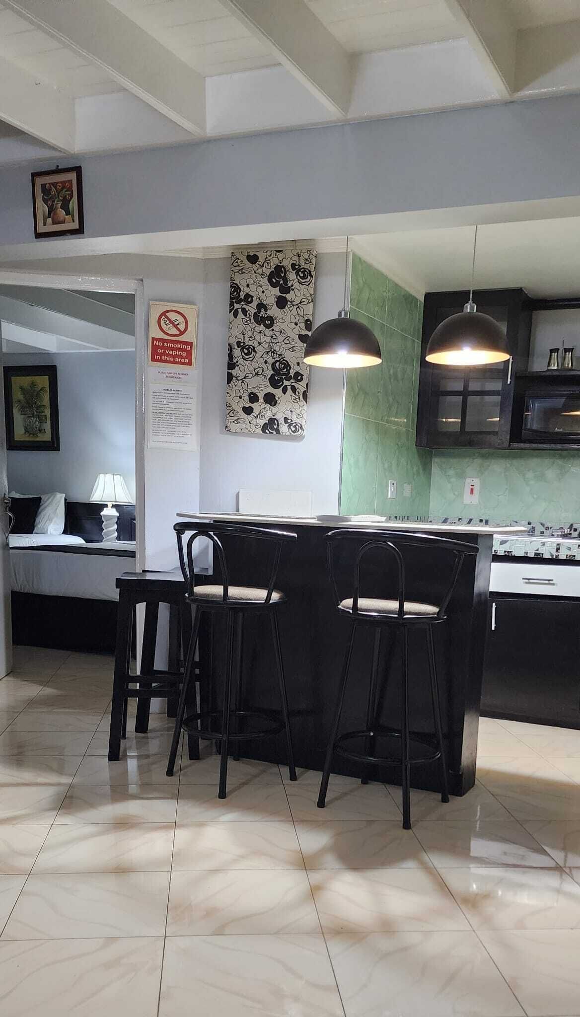 Une cuisine moderne avec un coin repas, comprenant une table et des chaises noires, un luminaire suspendu et un revêtement mural vert.
