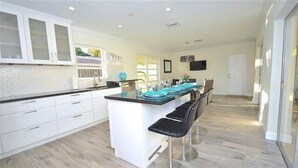 A modern kitchen with white cabinets, a large island with bar stools, and a dining area with a table set for four. - BY THE SEA VACATION VILLAS 4 BED PRIVATE POOL/BEACH NEAR-LBTS gated community (Lauderdale by the Sea)