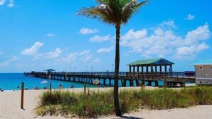 A beach with a palm tree, a pier, and a lifeguard tower. - BY THE SEA VACATION VILLAS 4 BED PRIVATE POOL/BEACH NEAR-LBTS gated community (Lauderdale by the Sea)