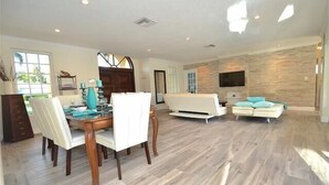 A spacious living room with a dining area, a sofa, and a TV mounted on the wall. - BY THE SEA VACATION VILLAS 4 BED PRIVATE POOL/BEACH NEAR-LBTS gated community (Lauderdale by the Sea)