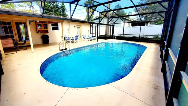 A covered swimming pool with a sunshade, lounge chairs, and a patio area with a table and chairs. - Experience the comfort you deserve while on vacation! (Deltona)