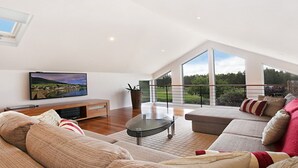 Un salon spacieux doté d’une grande télévision, de sièges confortables et d’un balcon offrant une vue agréable.