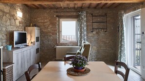 A rustic stone-walled room with a wooden table, chairs, a television, and a window with patterned curtains. - Apartment in renovated farmhouse in typical Chianti Tuscan village (Villa A Sesta)