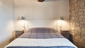 A bed with a quilted headboard, two bedside tables with lamps, and a stone wall. - Apartment in renovated farmhouse in typical Chianti Tuscan village (Villa A Sesta)