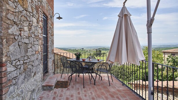 A terrace with a stone wall, a table with chairs, and a view of the countryside. - Apartment in renovated farmhouse in typical Chianti Tuscan village (Villa A Sesta)