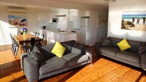 A modern living room with two grey sofas, a wooden coffee table, and a dining area with a wooden table and chairs.