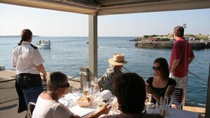 A group of people dining at an outdoor table with a view of the sea.