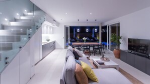 A modern living space with a glass staircase, a dining area with blue chairs, a sofa with cushions, and a TV on the right wall. - Koras Villa - Modern designed villa with heated pool - few steps from the beach  (Kaštel Stari)