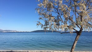 A tree-lined beach with clear blue water and a distant mountain range. - Koras Villa - Modern designed villa with heated pool - few steps from the beach  (Kaštel Stari)