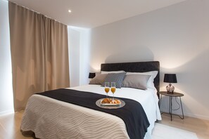 A modern hotel room with a large bed, a bedside table with a lamp, and a tray with croissants and juice glasses. - Koras Villa - Modern designed villa with heated pool - few steps from the beach  (Kaštel Stari)