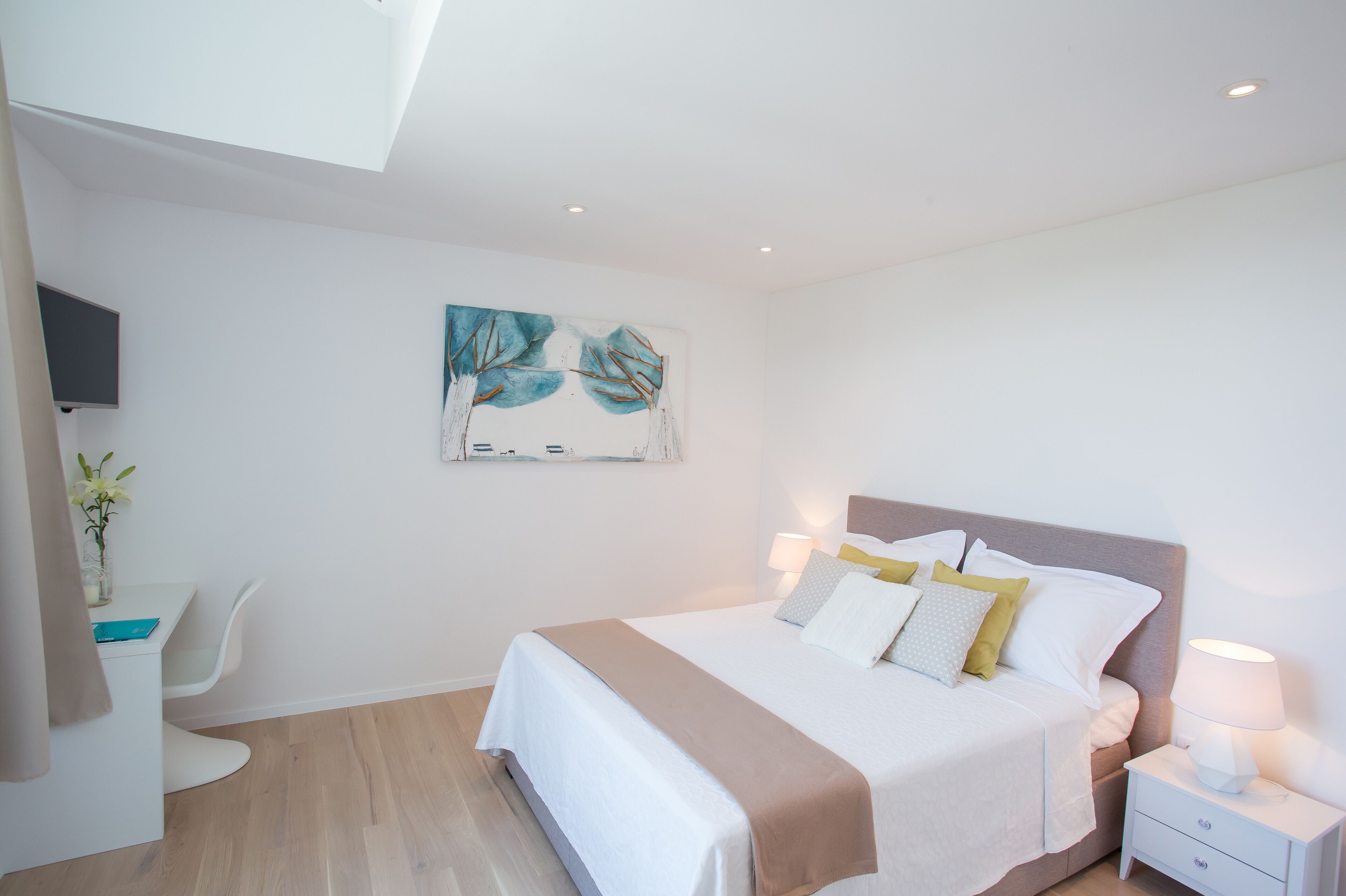 A modern bedroom with a bed, bedside table, and a painting on the wall.
