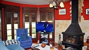 A living room with a blue sofa, a television, a fireplace, and wooden shutters. - Fantastic villa of 200 m2 in Siero (Asturias) (FORFONTIA)
