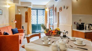 A hotel room with a dining area, a sofa, a table set for breakfast, and a kitchen area. - Suite with a Balcony at the Teatro Massimo (Catania)