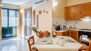 A modern kitchen with wooden cabinets, a dining table set for four, and a fruit bowl on the counter. - Suite with a Balcony at the Teatro Massimo (Catania)