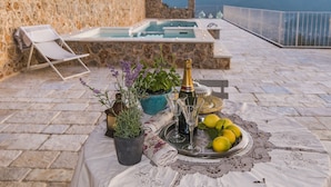 A stone patio with a pool, a table with a bottle, glasses, and lemons, and a chair.