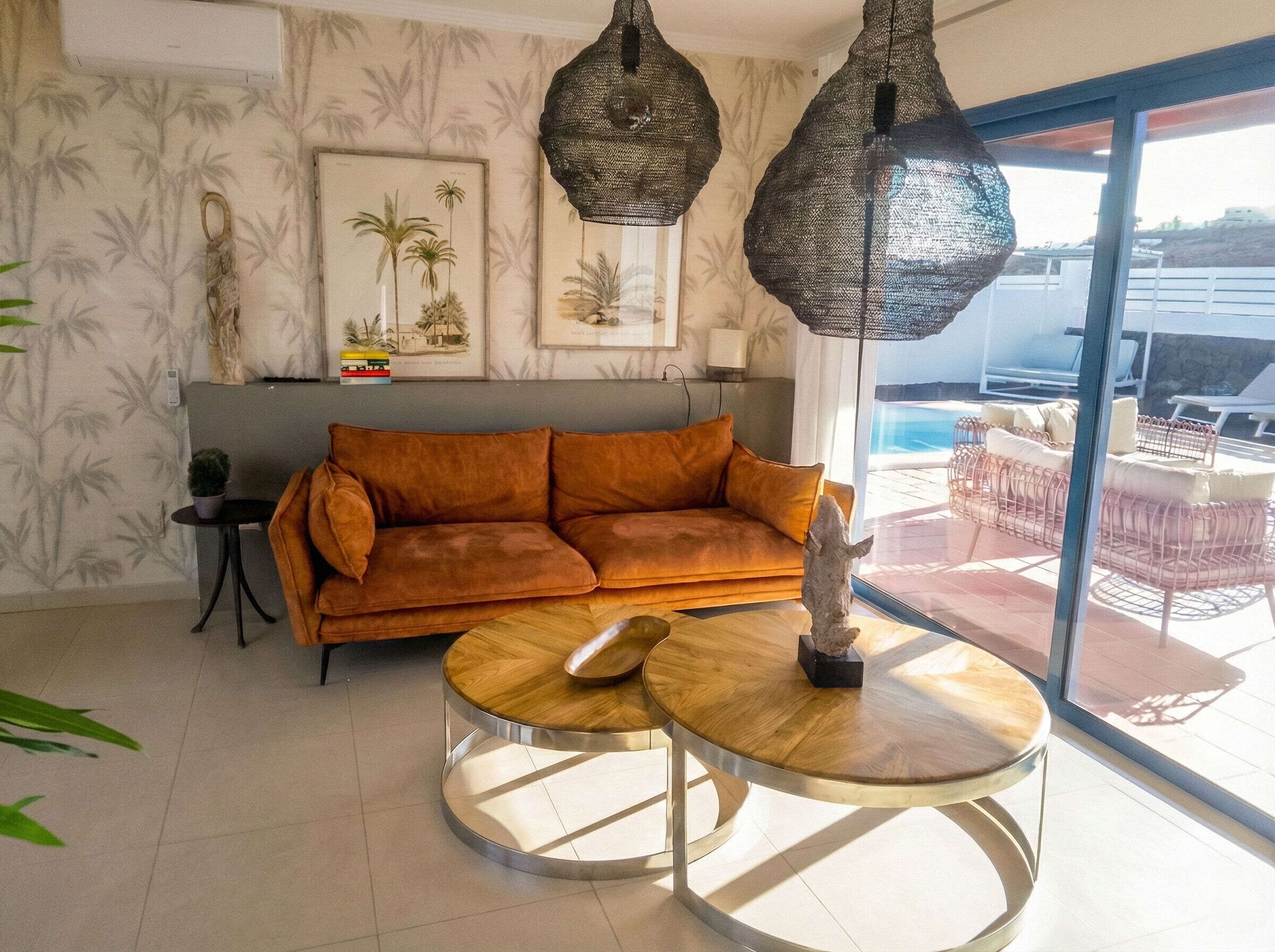 A modern living room with a brown sofa, a round wooden coffee table, and a large window overlooking a pool area.