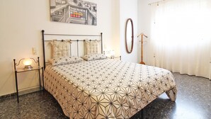A bedroom with a bed, a nightstand, a wall clock, a framed picture, and a window with curtains.