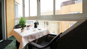 A balcony with a table set for two, a potted plant, a coffee pot, and a cup.