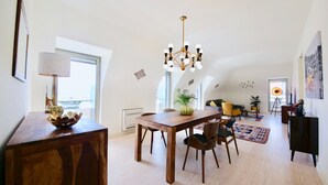 Een ruime woonkamer met een houten eettafel, stoelen, een kroonluchter en een groot raam.