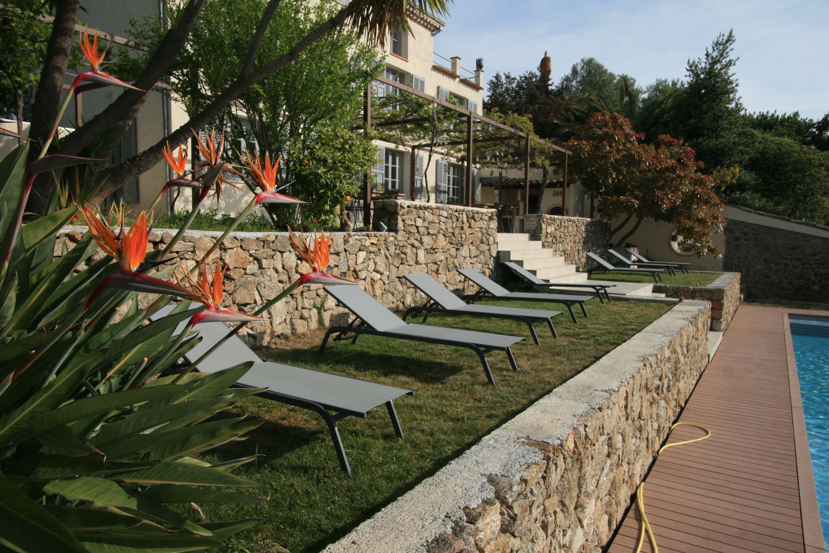 Un área junto a la piscina con sillones de descanso y un muro de piedra.