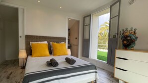 A bedroom with a bed, a nightstand, a lamp, a dresser, and a view of the outdoors.