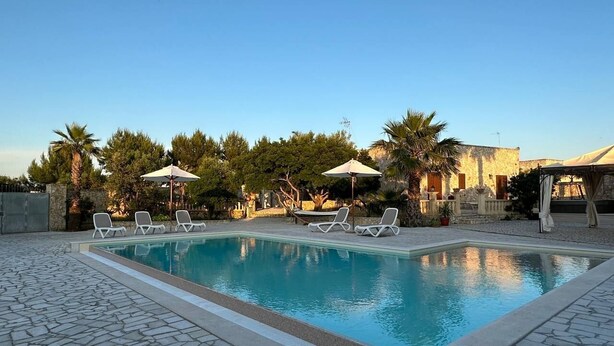 Ein Swimmingpool mit Liegestühlen und Sonnenschirmen, umgeben von Bäumen und einer Steinterrasse.