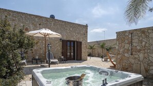 Ein Whirlpool in einem von Steinmauern umgebenen Außenbereich mit Holzterrasse, einem Patio-Tisch und einem Liegestuhl.