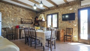 Ein Essbereich mit Steinsandsteinwänden, gedeckter Tafel für sechs Personen, Holzsesseln, einem an der Wand befestigten Fernseher und einem Fenster, das für natürliches Licht sorgt.