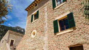 Un edificio de piedra con múltiples ventanas y puertas, plantas en macetas al frente, y un cielo despejado.
