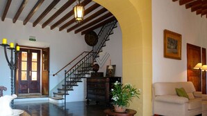 Un vestíbulo amplio con una escalera, un sofá blanco, una planta en maceta y un candelabro.