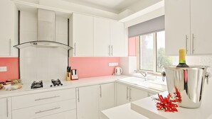 A modern kitchen with white cabinets, a gas stove, a stainless steel pot, and a window with a view. - Villa Georgios Rafaela: Secluded, pool, Wifi, A/C, sleeps 10 (Goudi Polis)