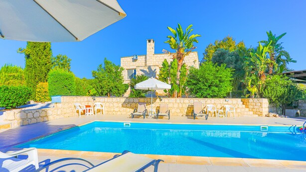 A swimming pool with lounge chairs and umbrellas, surrounded by stone walls and greenery. - Villa Georgios Rafaela: Secluded, pool, Wifi, A/C, sleeps 10 (Goudi Polis)