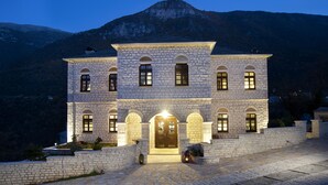Un bâtiment en pierre avec une entrée centrale, de nombreuses fenêtres et une chaîne de montagnes en arrière-plan.
