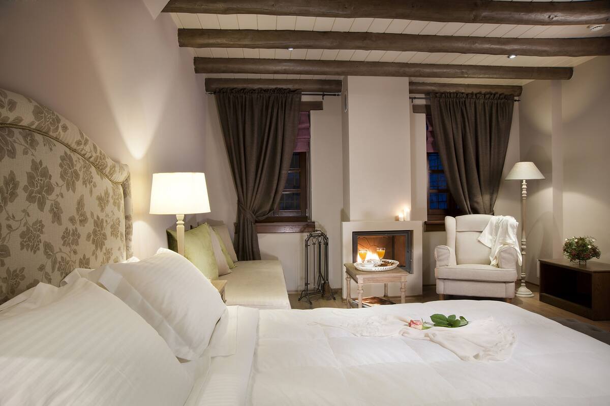 Een hotelkamer met een bed, een stoel, een klein tafeltje met een dienblad glazen en een open haard.