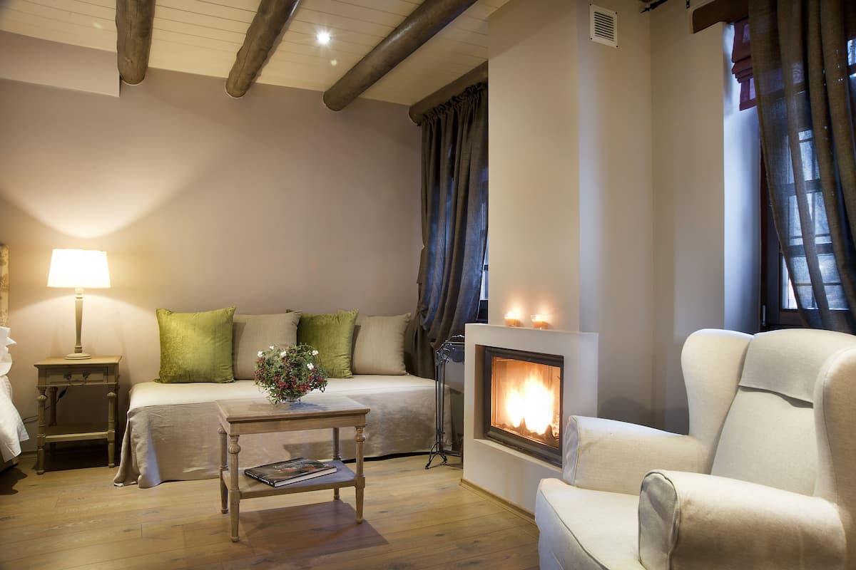 Een gezellige kamer met een bed, een tafel met een vaas, een stoel, een open haard en een nachtkastje.