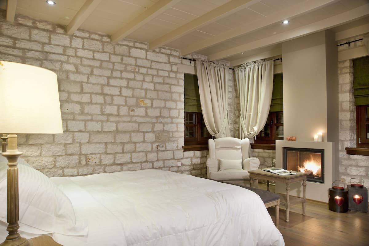 Een slaapkamer met een bakstenen muur, een bed, een stoel, een tafel en een open haard met kaarsen.