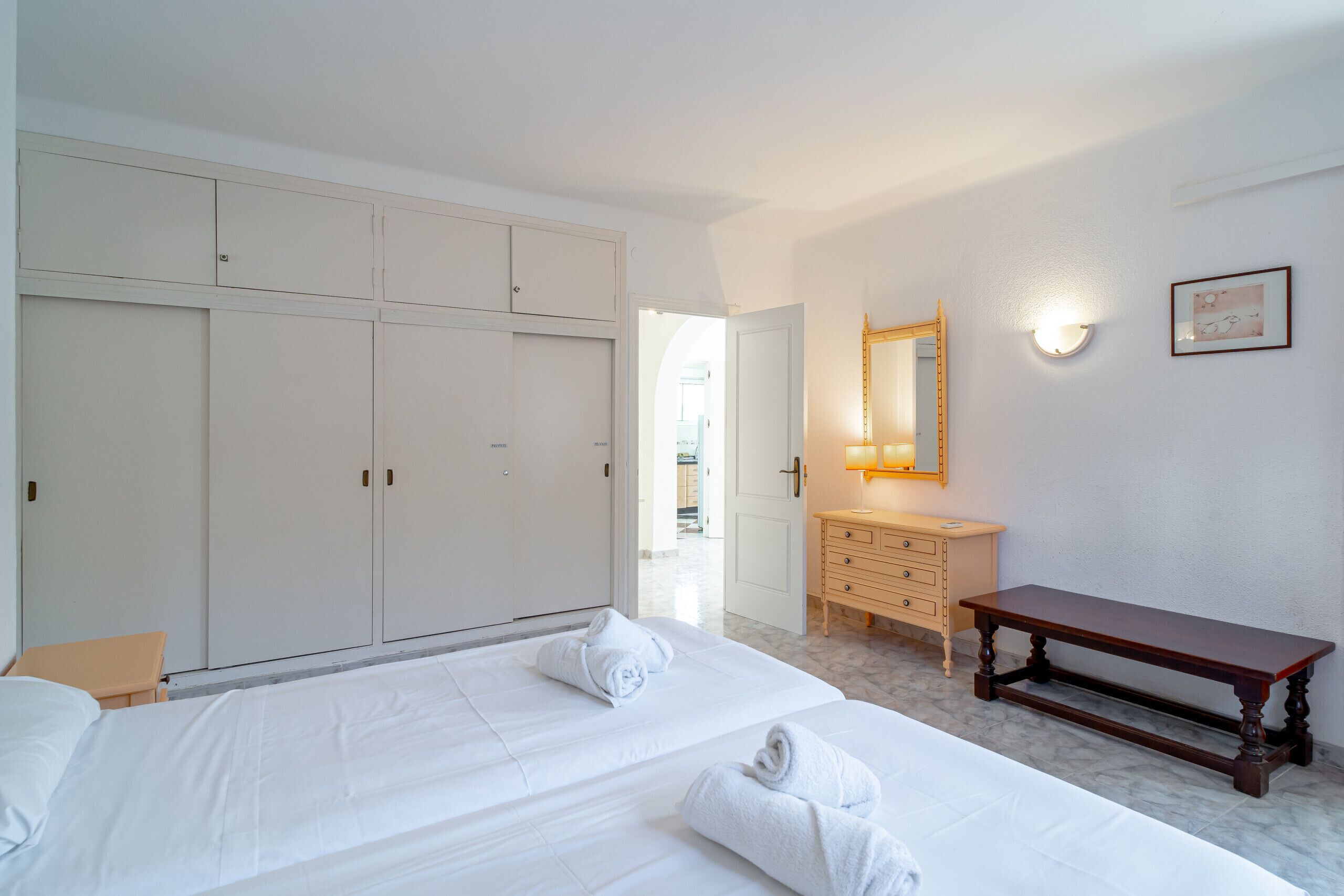 A hotel room with a large bed, a wooden bench, a dresser, and a mirror.