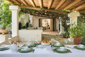 An outdoor dining area with a table set for a meal, surrounded by potted plants and a wooden pergola.