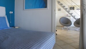 Quarto com cama, quadro, escrivaninha, cadeira e escada que leva a outro cômodo.