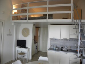Ein kompakter Wohnbereich mit Küchenzeile, Essplatz, Waschmaschine, Fernseher und Schlafkoje.