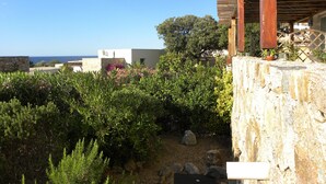 Um jardim com muro de pedra, pérgola de madeira e vista para o mar.