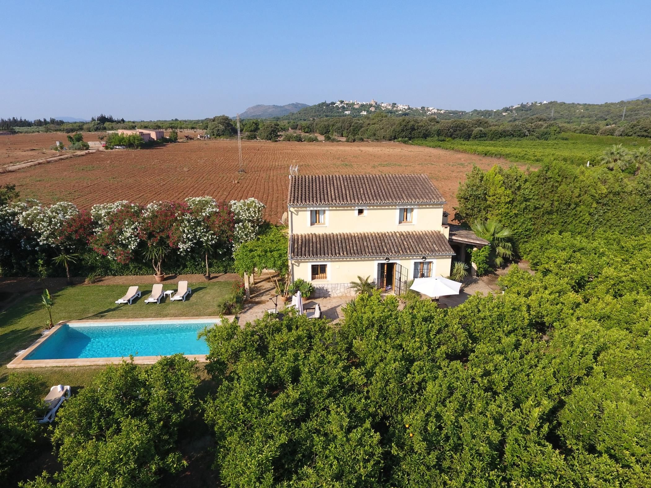 Una casa de dos pisos con piscina, rodeada de abundante vegetación y campos.