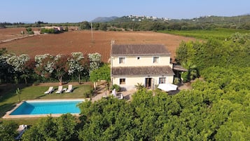 Una casa de dos pisos con piscina, rodeada de abundante vegetación y campos.